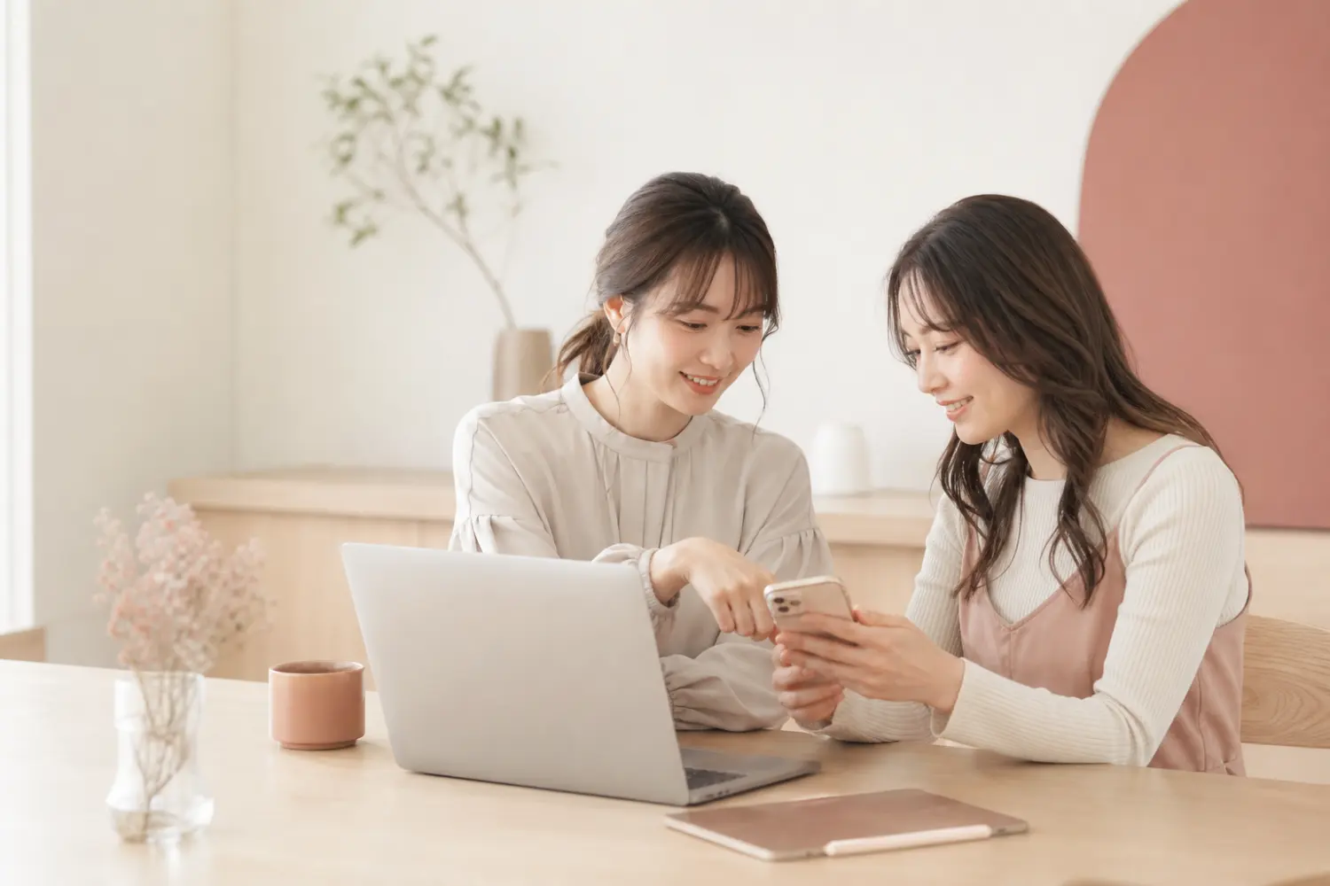 ノートパソコンとスマートフォンを見ながら一緒に確認する二人の女性